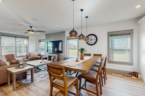 A spacious living area with a wooden dining table, comfortable seating, a ceiling fan, and large windows with blinds. - Gorgeous coastal home with plenty of space, shared pool  and easy beach access (Mexico Beach)