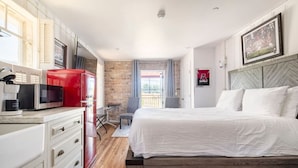 A modern hotel room with a bed, a desk with a red cabinet, a microwave, and a view of the outdoors.