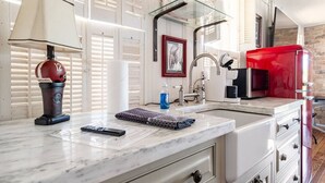 A kitchen with a marble countertop, a red refrigerator, a coffee machine, and a sink with a faucet.