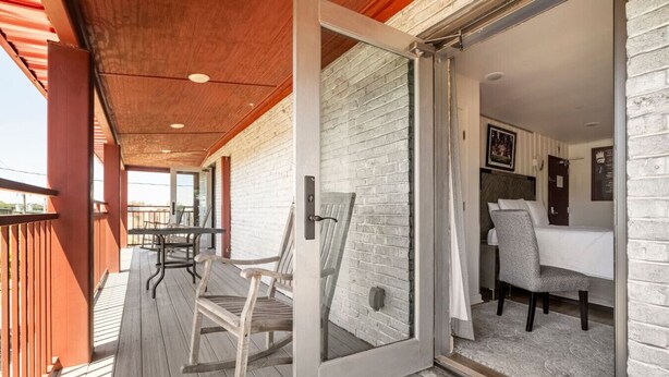 A wooden deck with a glass door leading to a room with a bed and a chair.