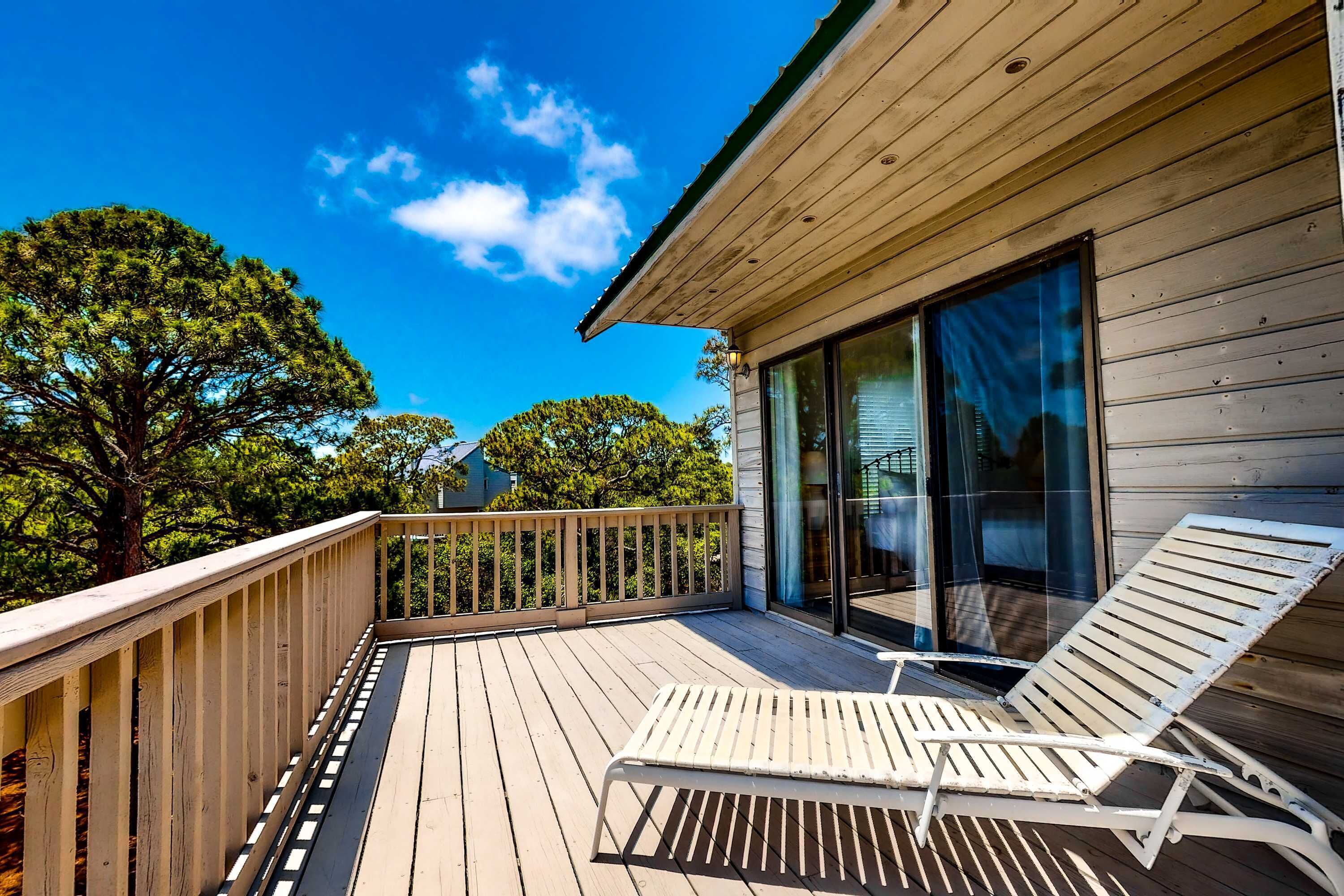 A wooden deck with a white sun lounger and a glass door leading to a room.