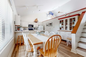 A spacious kitchen with white cabinets, a wooden dining table, and a staircase with a red railing. - Dog-friendly home near the beach with beach gear, on-site pool & tennis (St. George Island)