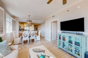 A living room with a dining area, a TV, and a bookshelf. - floor condo with hot tub, outdoor pool, gym, partial ocean views, balcony (Fort Walton Beach)