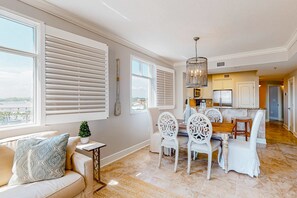 A spacious living area with a dining table and chairs, a sofa with a patterned cushion, and large windows with blinds. - floor condo with hot tub, outdoor pool, gym, partial ocean views, balcony (Fort Walton Beach)