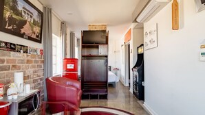 A narrow hallway with a red leather chair, a red filing cabinet, and a white bed in the background. - Alabama Boutique Hotel: #6 w/ TV Rm, PacMan Arcade (Tuscaloosa)