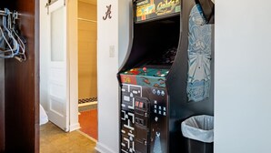 A room with a claw machine arcade game, a coat rack, and a door leading to a bathroom. - Alabama Boutique Hotel: #6 w/ TV Rm, PacMan Arcade (Tuscaloosa)