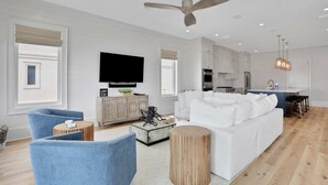 A modern living room with a white sofa, blue armchair, and a flat-screen TV. - Newly constructed beachfront home with panoramic bay & Gulf views (St. George Island)