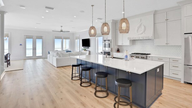 A modern kitchen with a large island, pendant lights, and a view to the living area. - Newly constructed beachfront home with panoramic bay & Gulf views (St. George Island)