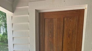 Una puerta de madera con marco blanco, un escalón que lleva a ella y un interruptor de luz en la pared a la izquierda.