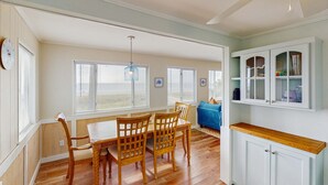 Un comedor con mesa y sillas de madera, una lámpara colgante azul y un armario blanco con puertas de cristal.