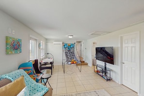 A living room with a sofa, a chair, a TV, a staircase, and a door. - Coastal escape with bay views, fishing, Washer / dryer, and Wifi (Eastpoint)