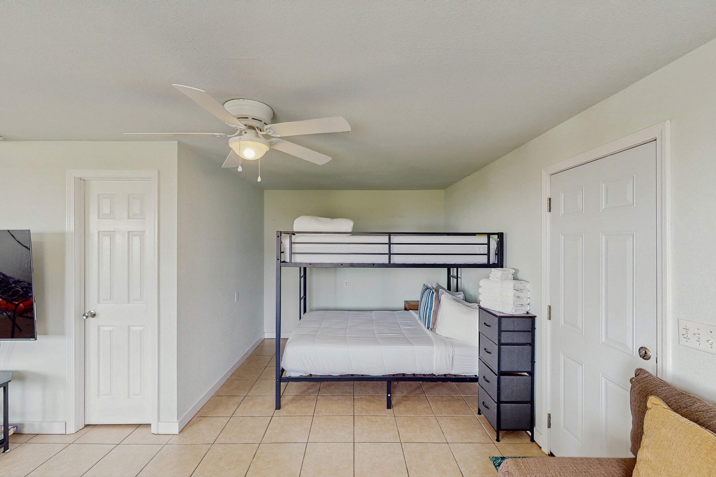 Una habitación con literas, ventilador de techo, escritorio y cómoda.
