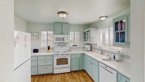 Una cocina con armarios verde claro, un refrigerador blanco, un microondas, un horno y un lavavajillas.
