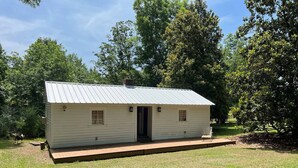 A small, single-story cabin with a metal roof and a front door, surrounded by a grassy yard and trees. - 2 of 3 GuestQuarters & 35 Min to U of Alabama (Eutaw)