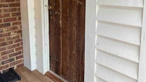 A wooden door with a metal handle, a white exterior wall, and a brick wall to the left. - 2 of 3 GuestQuarters & 35 Min to U of Alabama (Eutaw)