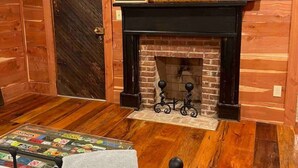 A cozy room with wooden walls, a fireplace, and a bed with a blanket labeled "ERS". - 2 of 3 GuestQuarters & 35 Min to U of Alabama (Eutaw)