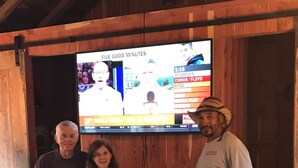 Three people standing in front of a television displaying a sports game. - Pecan Shelling House - 35 Mins to Univ of Alabama (Eutaw)