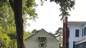 A small, single-story building with a star emblem on the front, surrounded by lush greenery and a large tree. - Pecan Shelling House - 35 Mins to Univ of Alabama (Eutaw)