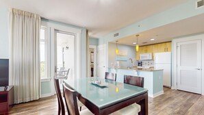 A modern kitchen with a central island, a dining area with a glass table, and a living room with a TV and curtains. - Golf-course & water-view condo with central AC, shared pool,hot tub (Miramar Beach)