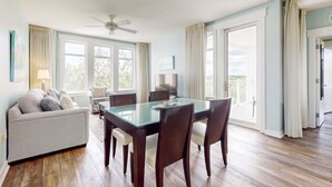 A spacious living area with a glass-top dining table, dark wooden chairs, a grey sofa, and a ceiling fan. - Golf-course & water-view condo with central AC, shared pool,hot tub (Miramar Beach)