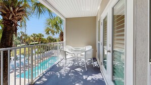 A balcony with white wicker furniture, a pool, and palm trees. - Bright, open 3rd-floor condo with pool views from private balcony - next to beach (Santa Rosa Beach)