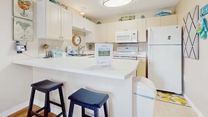A kitchen with white cabinets, a microwave, a refrigerator, and two bar stools. - Bright, open 3rd-floor condo with pool views from private balcony - next to beach (Santa Rosa Beach)