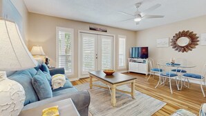 A living room with a sofa, coffee table, TV, and dining area with chairs and a table. - Bright, open 3rd-floor condo with pool views from private balcony - next to beach (Santa Rosa Beach)