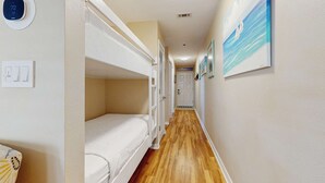 A narrow hallway with bunk beds, a thermostat, and a painting of a sailboat. - Bright, open 3rd-floor condo with pool views from private balcony - next to beach (Santa Rosa Beach)