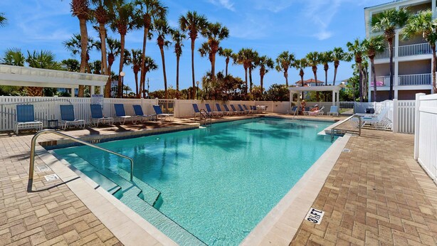A swimming pool with clear water, surrounded by palm trees and lounge chairs. - Bright, open 3rd-floor condo with pool views from private balcony - next to beach (Santa Rosa Beach)