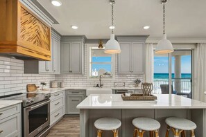 Una cocina moderna con una isla grande, muebles blancos y vistas al océano.