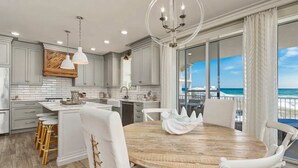 A modern kitchen with grey cabinetry, a wooden island, and a dining area with white chairs and a wooden table. - Stunning Beachfront condo with two pools, a hot tub, onsite gym and tennis/pickleball courts. (Santa Rosa Beach)