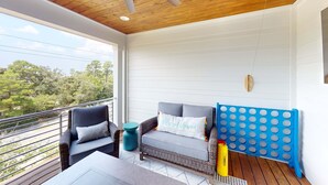 Een balkon met rieten meubilair, een plafondventilator en uitzicht op bomen.