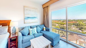 A modern living room with a sofa, a coffee table, and a view of a coastal landscape through large windows.