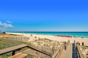 A beach with a wooden boardwalk leading to the shore, clear blue sky, and turquoise water.