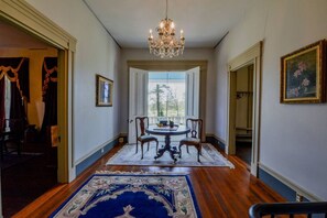 Un couloir orné d’un lustre, une table à manger avec des chaises et un grand tapis.