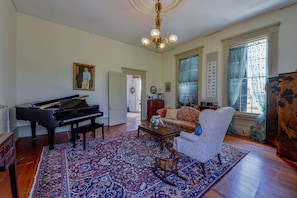 A spacious living room with a grand piano, a patterned rug, a sofa, and a chandelier.