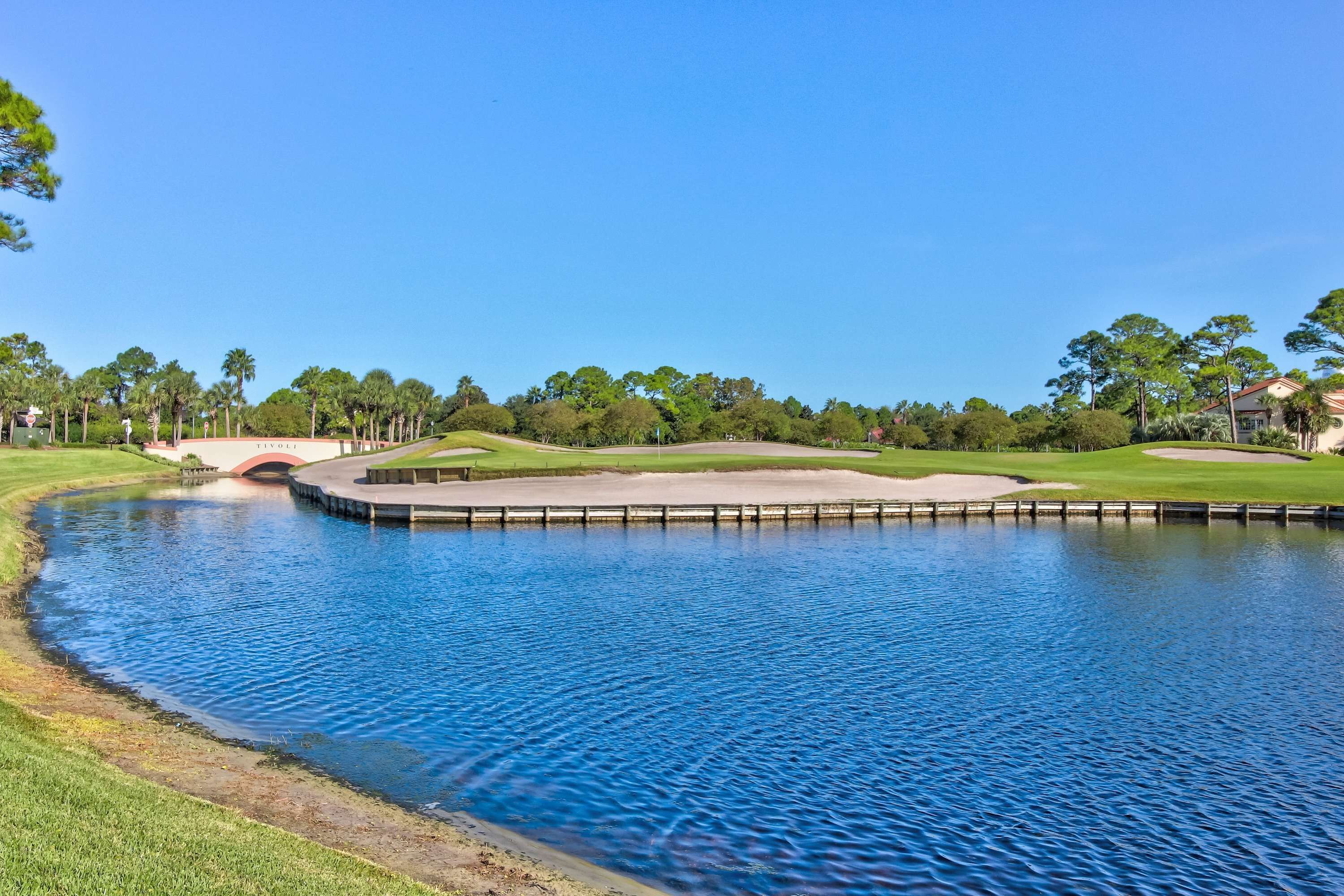 A golf course with a pond, a bridge, and a well-maintained lawn.