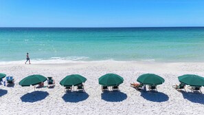 A beach with white sand, a clear blue sea, and several green umbrellas and beach chairs. - Inviting 5th Floor Condo On Okaloosa Island Gulf-Front Views Beach Chairs (Fort Walton Beach)