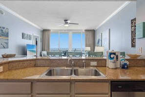 A kitchen with a double sink, a ceiling fan, and a view of the ocean through large windows. - Inviting 5th Floor Condo On Okaloosa Island Gulf-Front Views Beach Chairs (Fort Walton Beach)