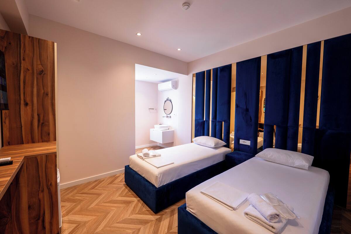 A hotel room with two beds, a wooden accent wall, a mirror, and a small bedside table.