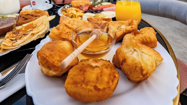 Colazione su un tavolo all'aperto con vista sulla città, che comprende un piatto di pasticcini, un bicchiere di succo d'arancia e una ciotola di miele.