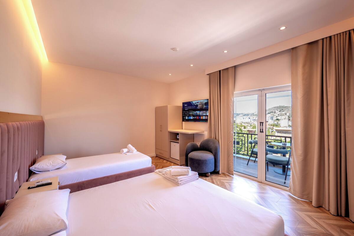 A hotel room with two beds, a TV, a desk, and a balcony with a view.