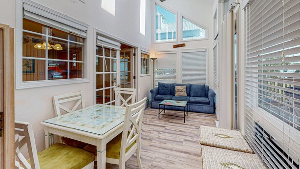 A bright, sunlit room with a dining table and chairs, a blue sofa, and large windows with blinds. - Gulf view home across the street from the beach - walk to shops,restaurants (Santa Rosa Beach)