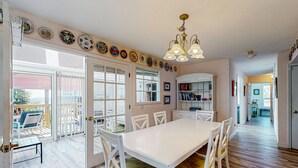 A spacious dining area with a white table and chairs, a ceiling fan, and a view of the outdoors through large windows. - Gulf view home across the street from the beach - walk to shops,restaurants (Santa Rosa Beach)