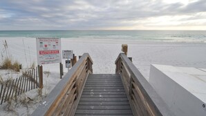 Eine Holztreppe führt zu einem Sandstrand, an dessen Seite ein Schild mit Warnflaggen angebracht ist.