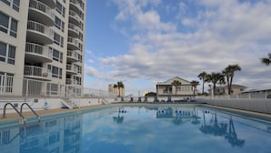 Ein Swimmingpool mit blauem Himmel und Wolken, umgeben von einem weißen Zaun und Palmen.