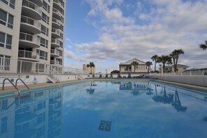 Ein Swimmingpool mit blauem Himmel und Wolken, umgeben von einem weißen Zaun und Palmen.