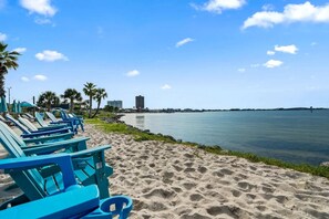 A beach with blue lounge chairs and a calm sea. - Sunlit & tropical beachfront condo with pool, gym, balcony views (Pensacola Beach)