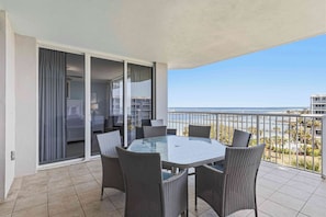 Un balcon avec une table en verre et des chaises en osier, une porte-fenêtre coulissante et une vue sur la mer et les bâtiments.