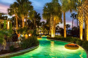 Une piscine entourée de palmiers et une terrasse en bois avec des chaises.